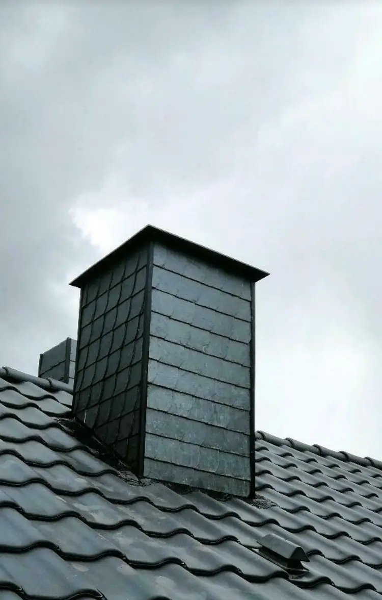 Ein schwarzer Schornstein auf einem Dach mit bewölktem Himmel.