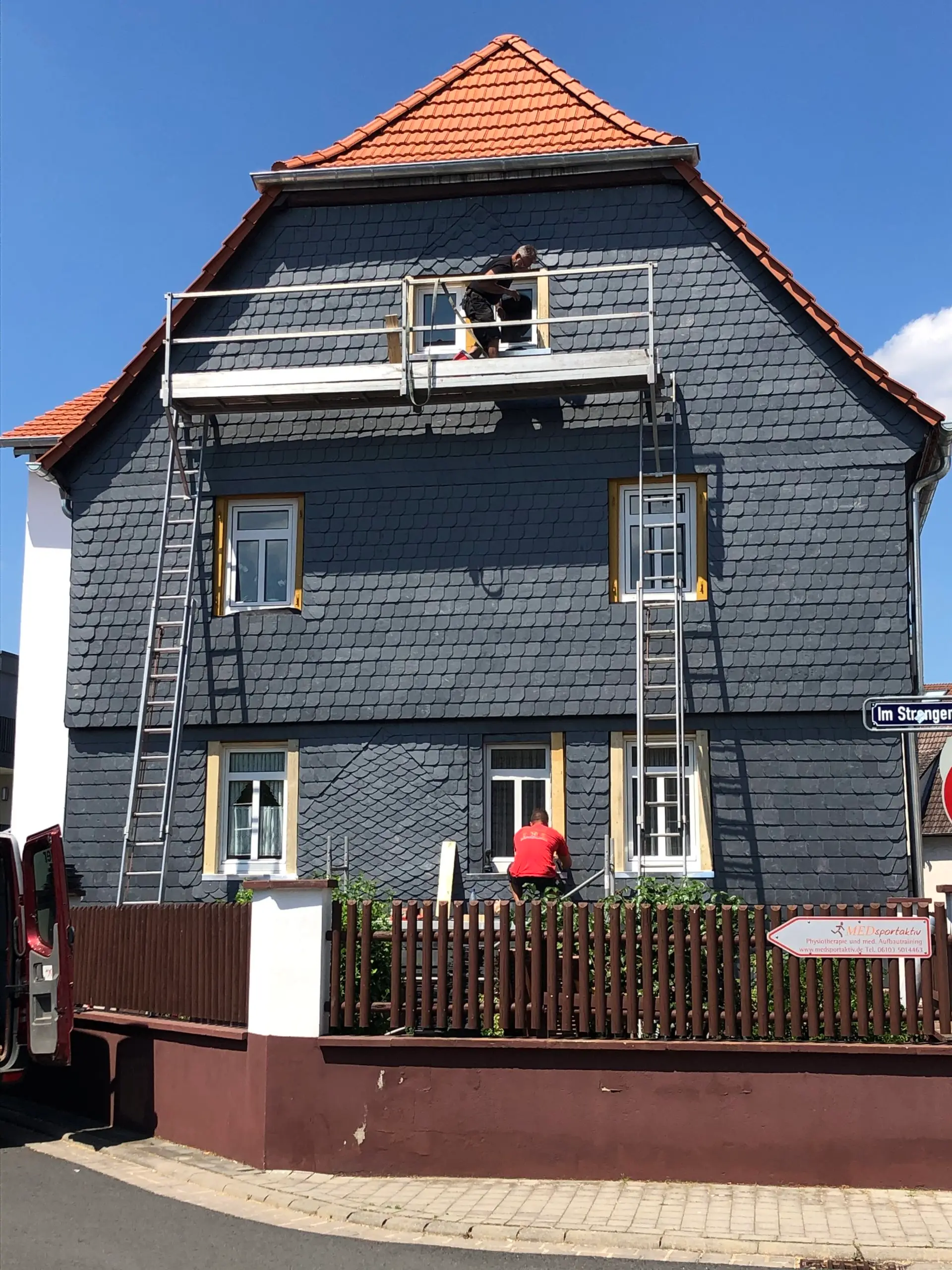 Ein Mann streicht auf einer Leiter ein Haus.