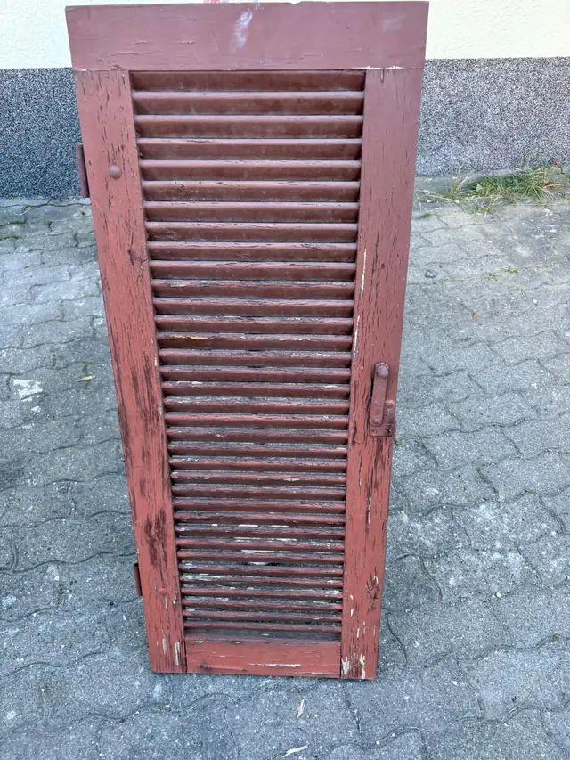 Hölzerner Fensterladen mit abgeblättertem rotem Lack.