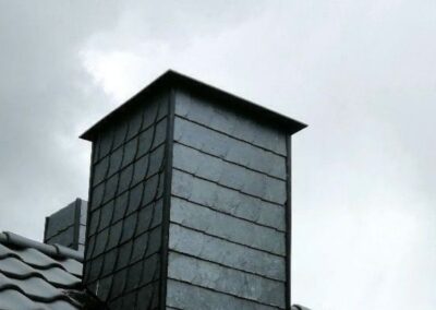 Ein schwarzer Schornstein auf einem Dach mit bewölktem Himmel.