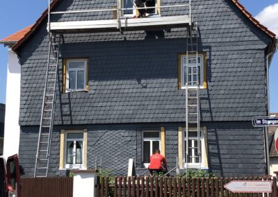 Ein Mann streicht auf einer Leiter ein Haus.
